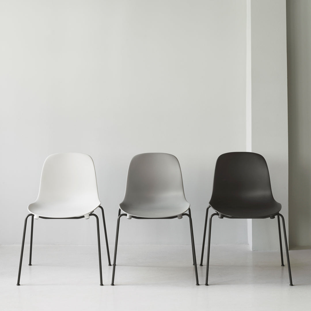 Set of three minimalist chairs in white, gray, and black, featuring smooth surfaces and sleek metal legs.