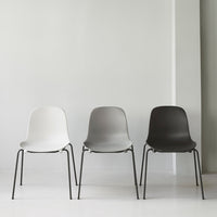 Set of three minimalist chairs in white, gray, and black, featuring smooth surfaces and sleek metal legs.