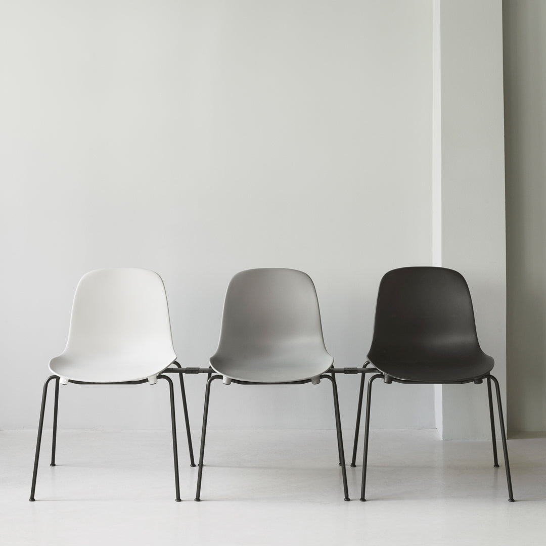 Set of three minimalist chairs in white, light gray, and dark gray with sleek black legs against a plain background.