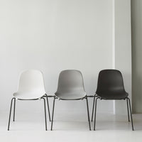 Set of three minimalist chairs in white, light gray, and dark gray with sleek black legs against a plain background.