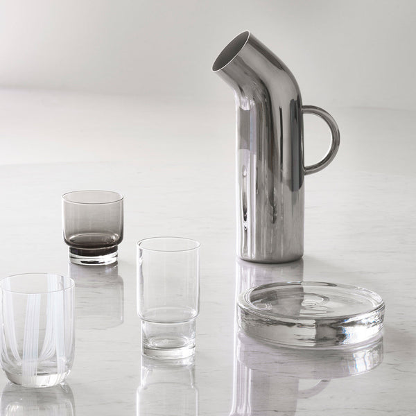 Metallic silver pitcher with mixed clear and smoky glasses; modern, minimalist design showcasing sleek lines and shapes.