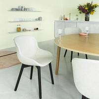Modern white dining chair with black legs against a pastel green backdrop, featuring simple, sleek lines and soft curves.