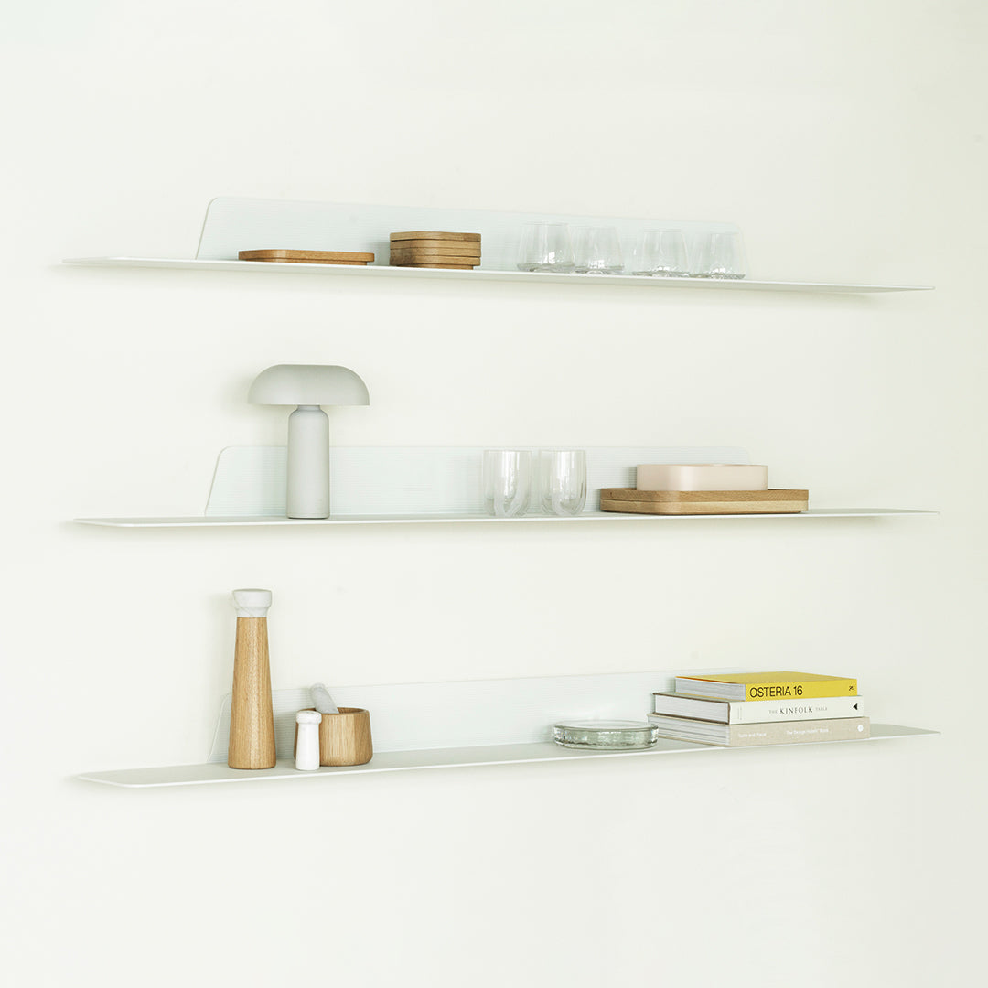 Clear glass shelves with warm wood accents and soft pastel items create a modern, minimalist display.