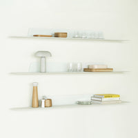 Clear glass shelves with warm wood accents and soft pastel items create a modern, minimalist display.