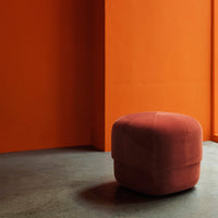 Soft velvet pouf in a rich terracotta color, set against a vibrant orange wall.