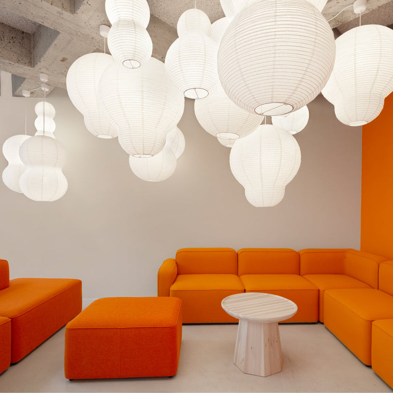 Orange sectional sofa with white paper lanterns and a light wood coffee table in a modern, bright space.