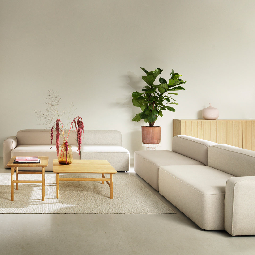 Modern beige sectional sofa with clean lines, paired with a natural wood coffee table and greenery accents.