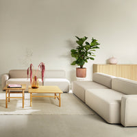 Modern beige sectional sofa with clean lines, paired with a natural wood coffee table and greenery accents.