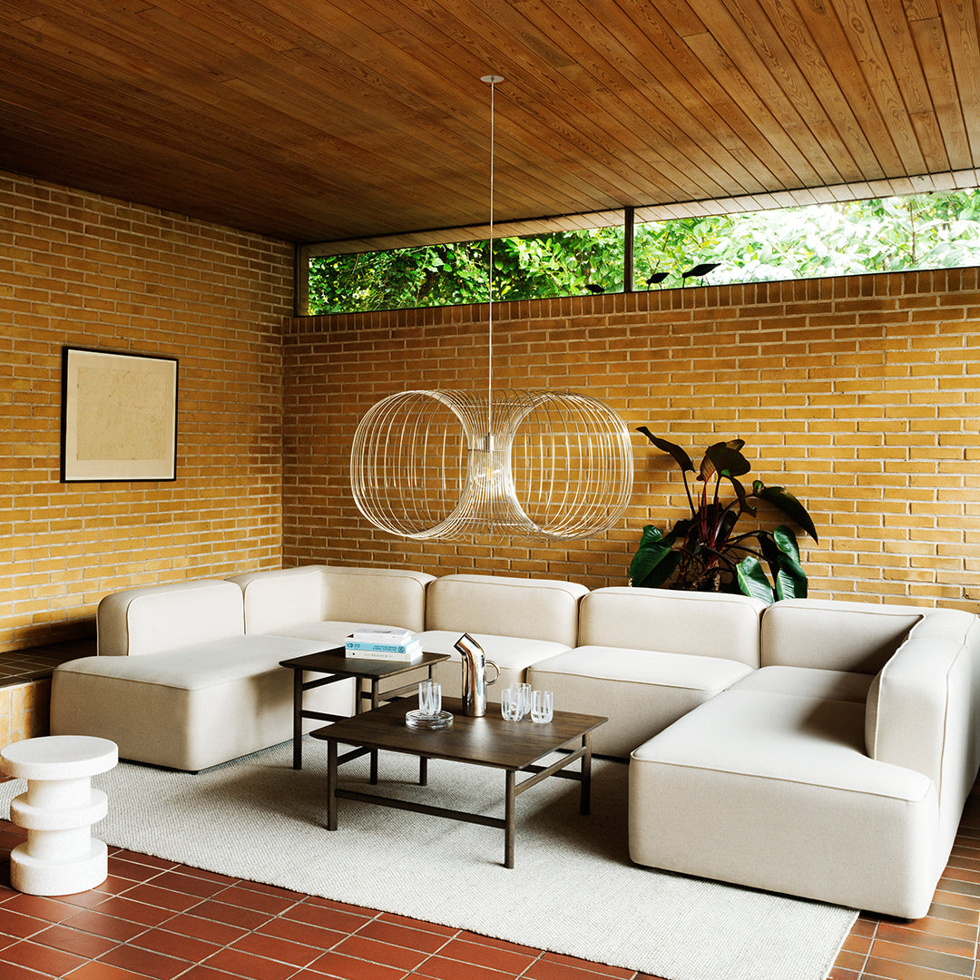 Beige sectional sofa with clean lines, textured white rug, and natural wood accents against a brick wall backdrop.