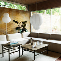 Neutral beige sofa, minimalist black coffee table, soft white pendant lights, and green plant accents in a bright, airy room.