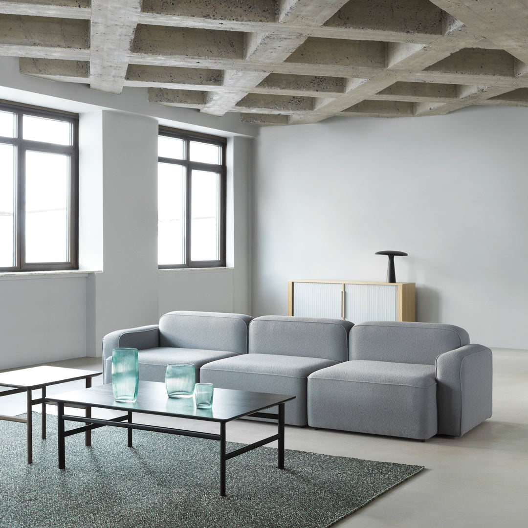 Light grey sectional sofa with a smooth fabric texture, paired with a dark metal coffee table and green rug for contrast.