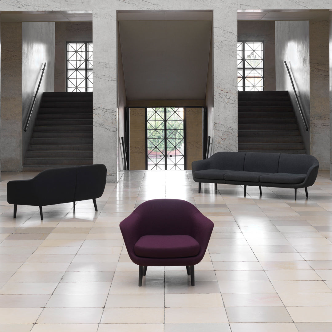 Modern seating collection featuring a deep purple chair and sleek black sofas against a light tiled floor.