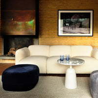 Cream sofa with velvet navy and grey poufs, round white table, and textured beige rug in a warm, modern setting.
