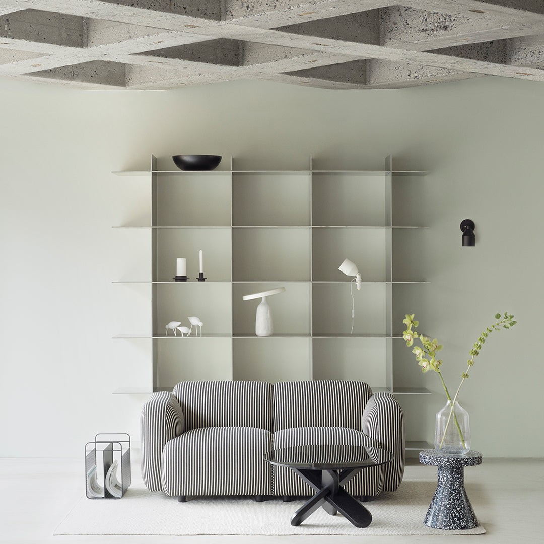 Gray textured sofa with a minimalist geometric pattern, set against a pale green wall and neutral decor elements.