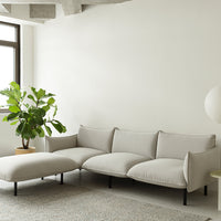 Light gray sectional sofa with smooth upholstery and minimalistic design, complemented by a green plant and neutral backdrop.