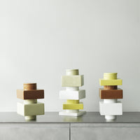 Colorful stacked vases in earthy brown, soft yellow, and crisp white against a minimalist background.