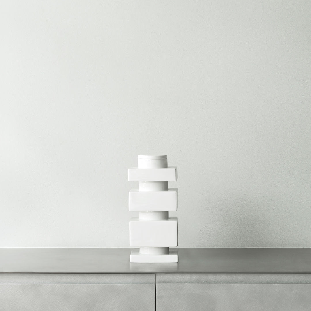 Modern white ceramic vase with stacked geometric shapes against a minimalist, light grey background.