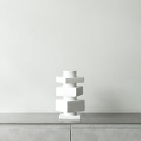White geometric vase with layered blocks on a sleek gray surface against a light gray wall. Modern minimalist design.