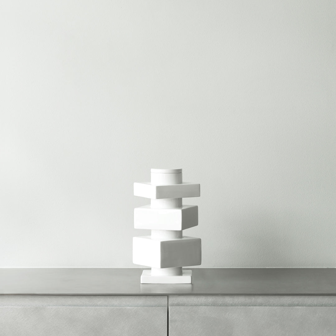 White geometric vase with layered blocks on a sleek gray surface against a light gray wall. Modern minimalist design.