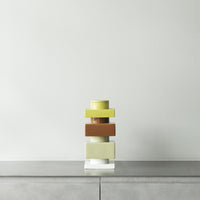 "Stacked decorative vases in soft yellow, green, and warm brown, with a modern glass base."