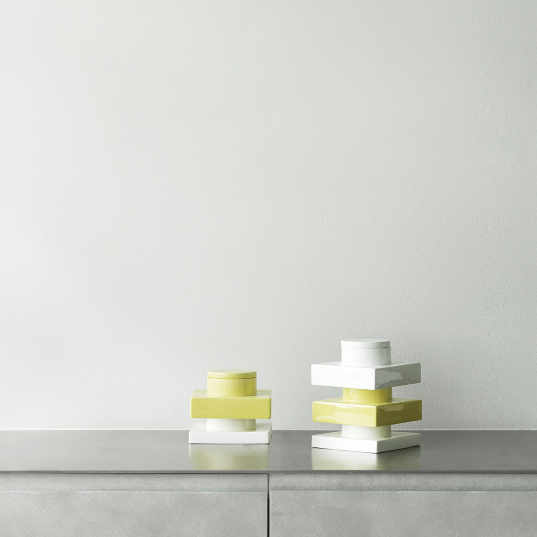 Stacked geometric decor in white and vibrant yellow on a minimalist gray surface against a neutral wall.