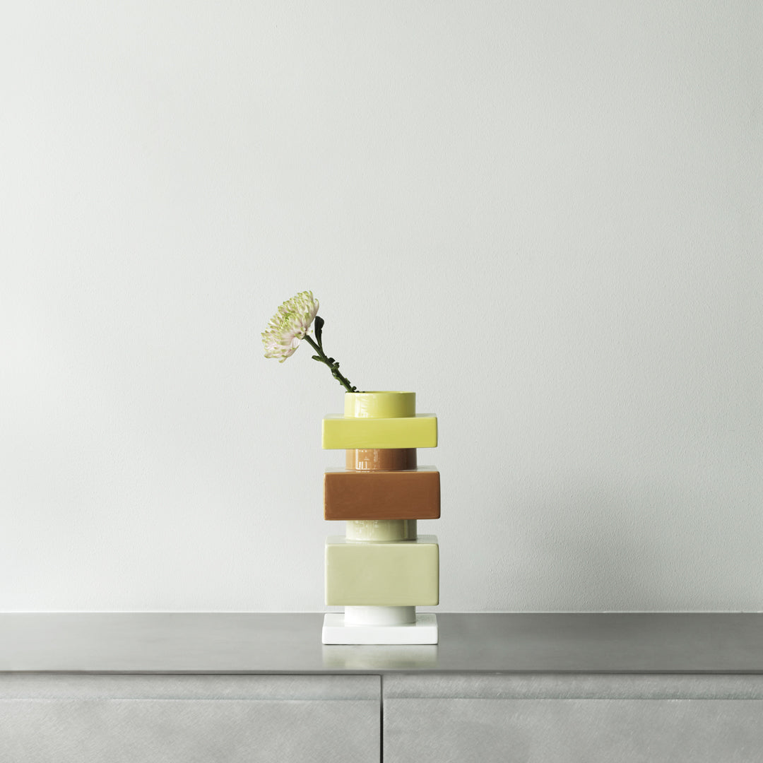 Colorful stacked vase in yellow, green, brown, and white with a single flower. Modern design and smooth patterns.