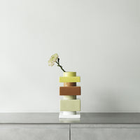 Colorful stacked vase in yellow, green, brown, and white with a single flower. Modern design and smooth patterns.