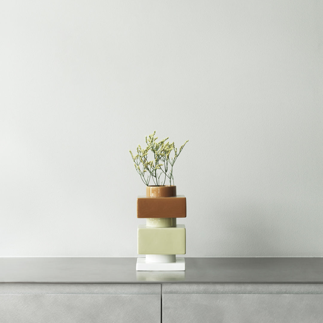 Modern stacked vase in muted green, terracotta, and clear glass with delicate greenery accent.