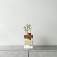Modern stacked vase in muted green, terracotta, and clear glass with delicate greenery accent.