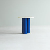 Round white tabletop on cylindrical blue legs, featuring a minimalist design against a light backdrop.