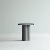 Round table with a speckled top in shades of gray and blue, featuring a minimalistic design with cylindrical legs.