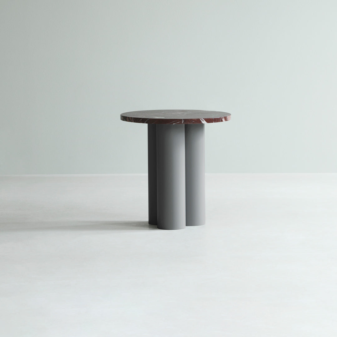 Round table with a gray base and a textured, dark red top against a light green background. Minimalist design.