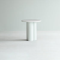 Round white table with a smooth surface and minimalist cylindrical base against a light gray background.