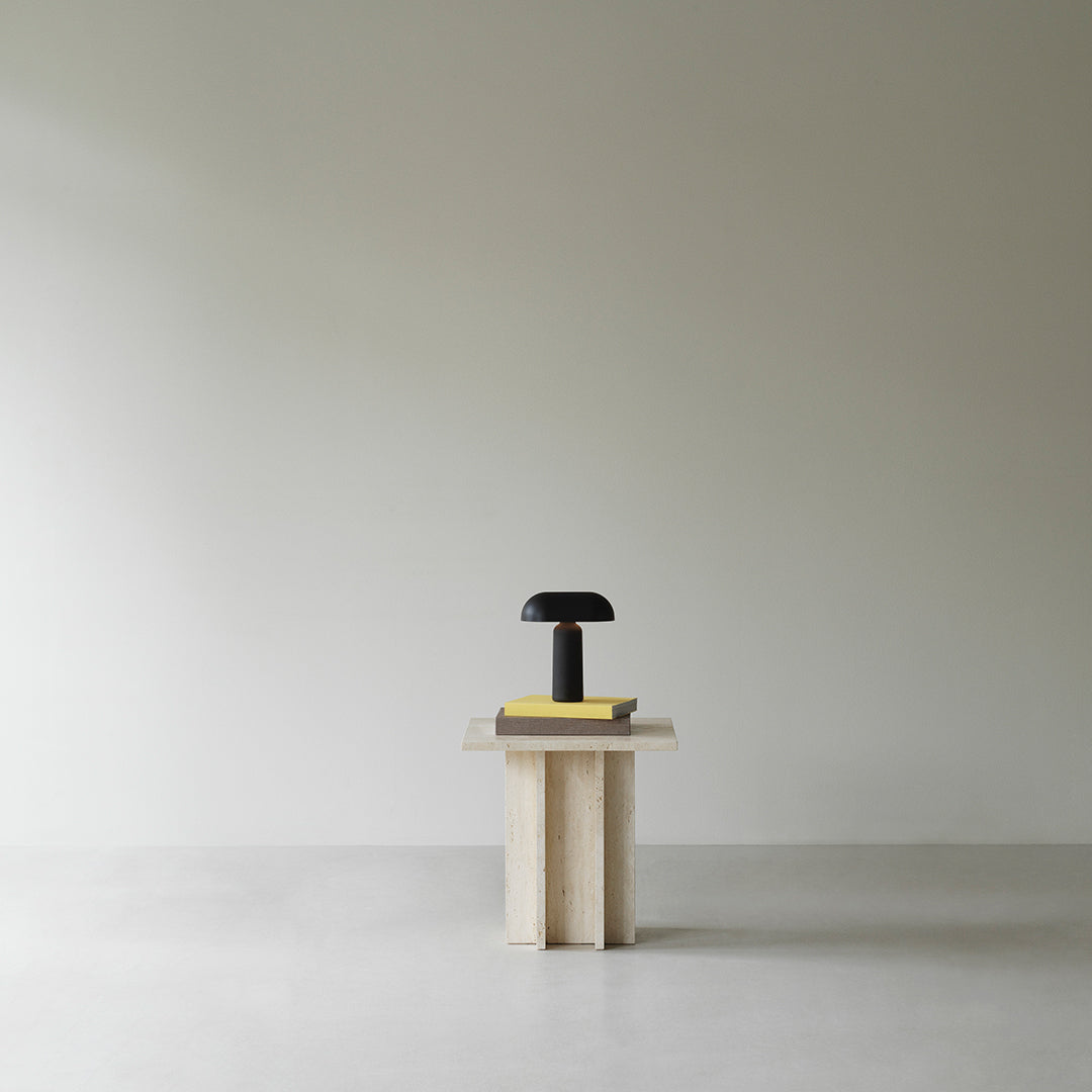 Minimalist black lamp on a light wooden table against a smooth, neutral wall background. Simple colors and clean design.