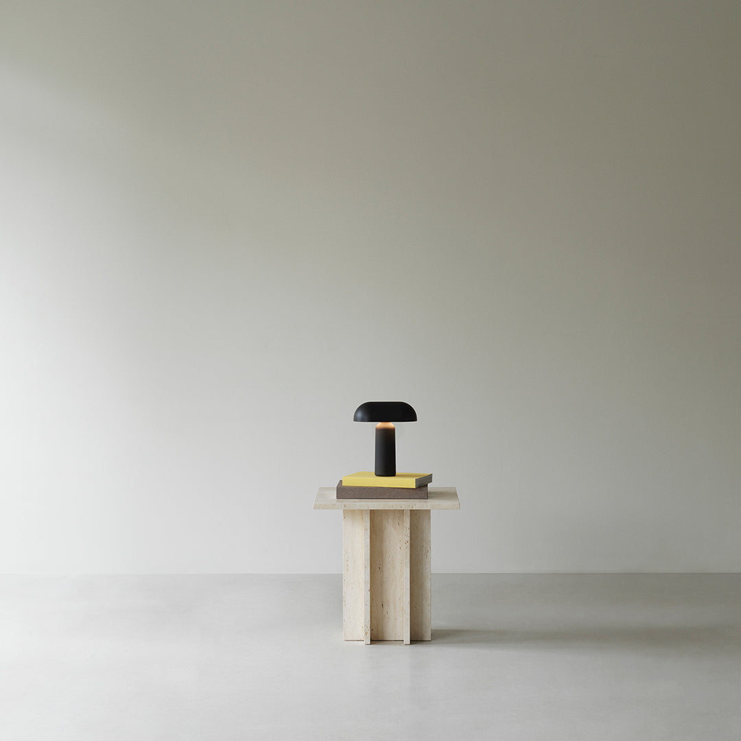 Black lamp on a light wooden table, featuring a minimalist design against a neutral background. Modern and sleek aesthetic.