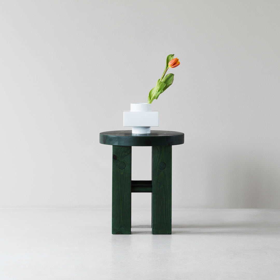 Green wooden table with a smooth, dark finish, featuring minimalist white vases and an orange flower.