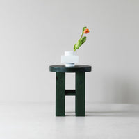 Green wooden table with a smooth, dark finish, featuring minimalist white vases and an orange flower.
