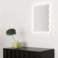 "Soft white scalloped mirror on a light wall, paired with a green planter on a black cabinet."