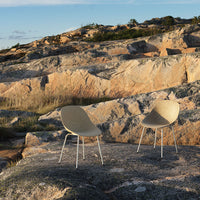 Beige modern chairs with simple, smooth curves set against a rugged rocky landscape under a clear blue sky.