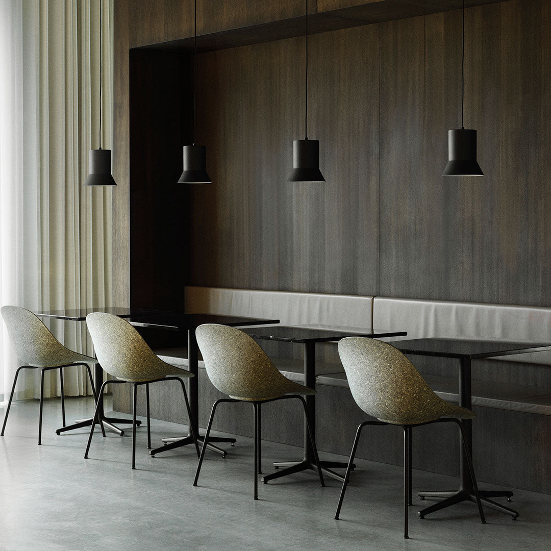 Minimalist dining space featuring muted beige chairs, sleek black tables, and contrasting black pendant lights against wood paneling.