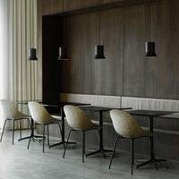 Minimalist dining space featuring muted beige chairs, sleek black tables, and contrasting black pendant lights against wood paneling.