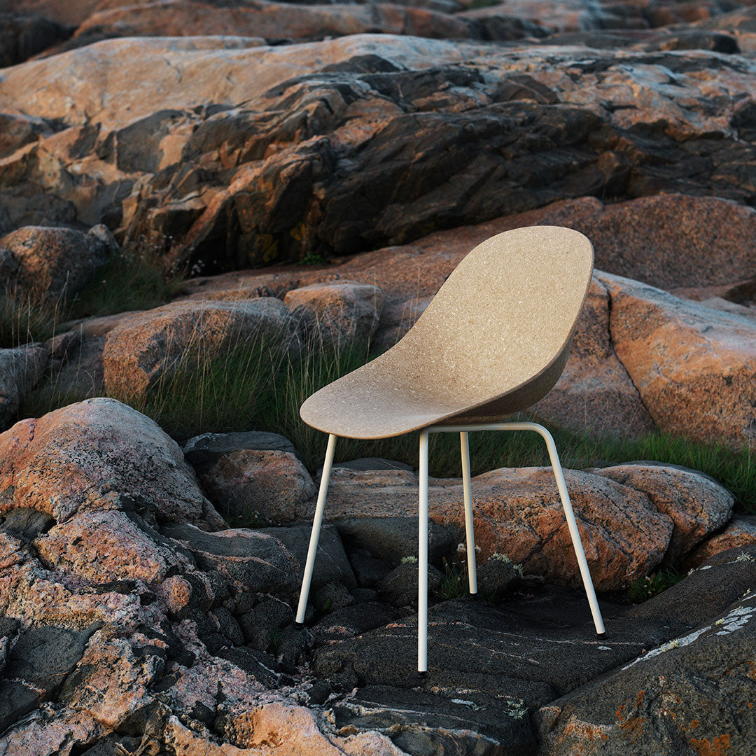 Cork-colored chair with a smooth, curved design, complemented by white metal legs, set against rocky terrain.