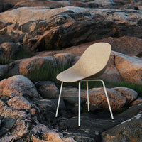 Cork-colored chair with a smooth, curved design, complemented by white metal legs, set against rocky terrain.