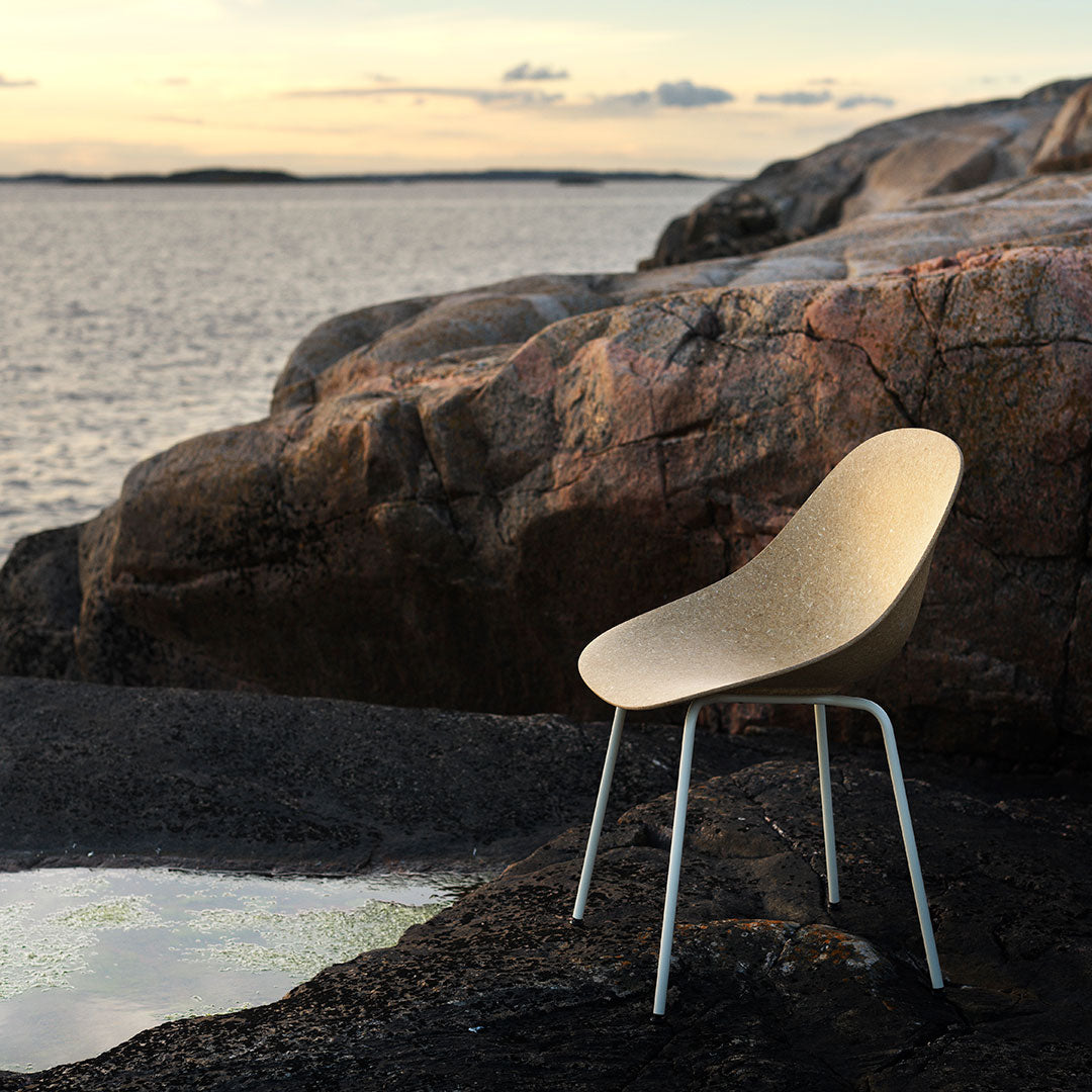 Modern beige chair with a smooth, minimalist design against a rugged, rocky landscape. Soft colors blend harmoniously.
