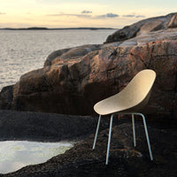 Modern beige chair with a smooth, minimalist design against a rugged, rocky landscape. Soft colors blend harmoniously.