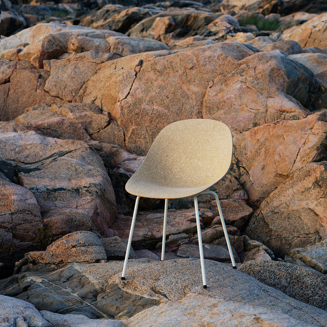 Beige chair with a smooth, contoured seat on silver legs, set against rugged rock textures.