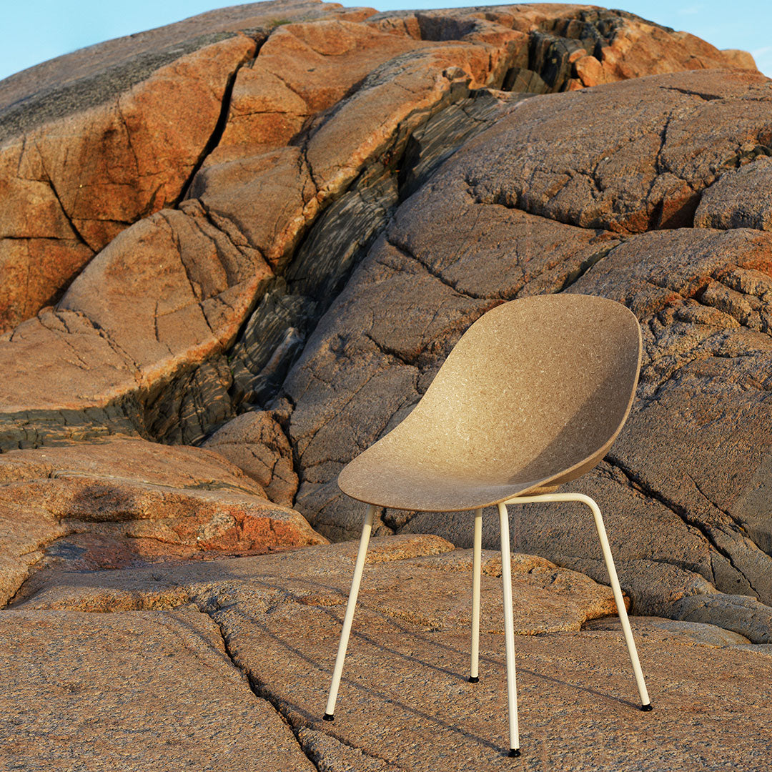 Sleek beige chair with a smooth texture, set against rugged, earthy-toned rocks, highlighting natural patterns.