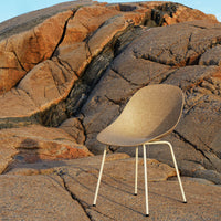 Sleek beige chair with a smooth texture, set against rugged, earthy-toned rocks, highlighting natural patterns.