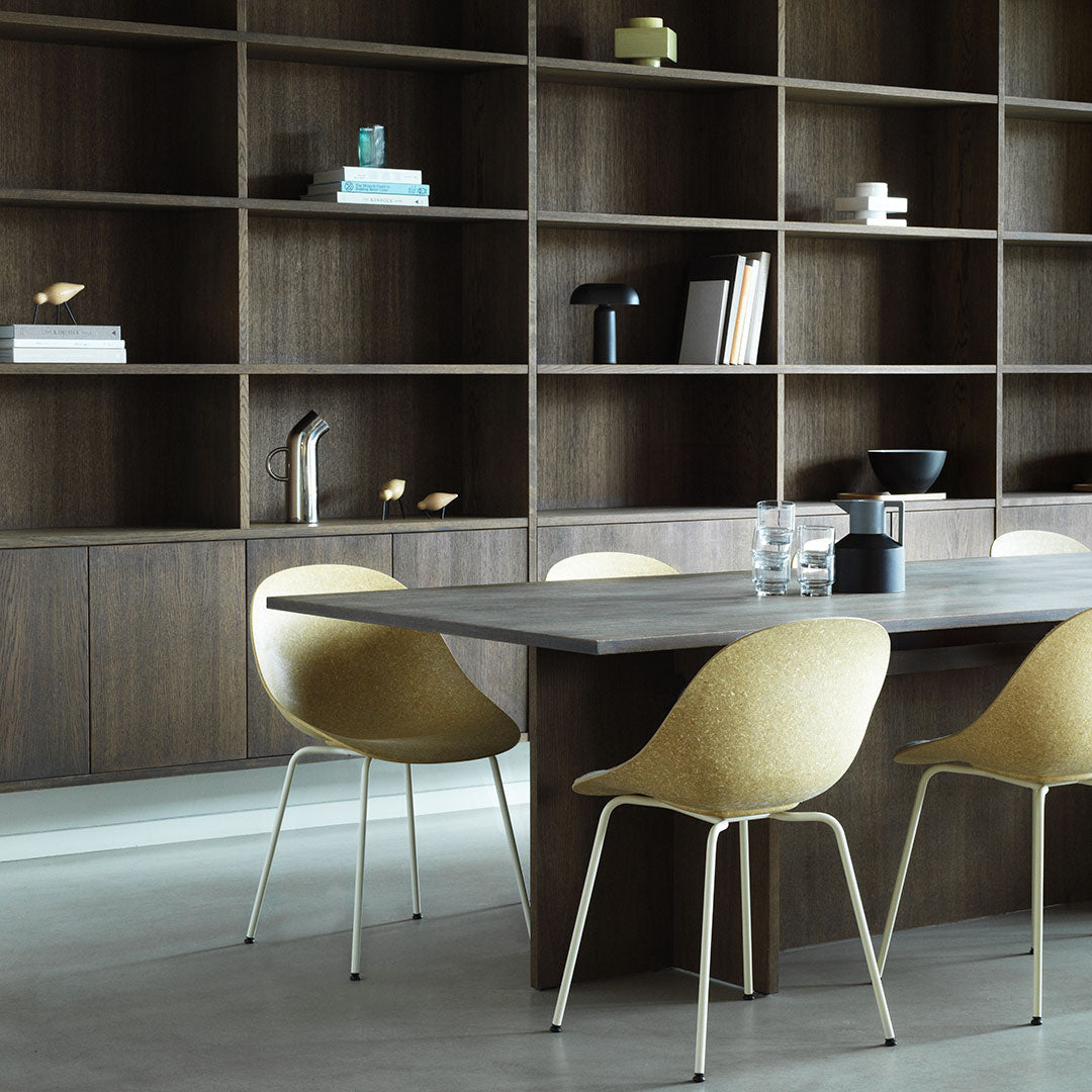 Modern dining area featuring a sleek wooden table, beige chairs, and a contrasting dark shelving unit.