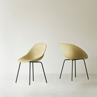 Minimalist beige chairs with sleek black metal legs, featuring a smooth, curved seat design.